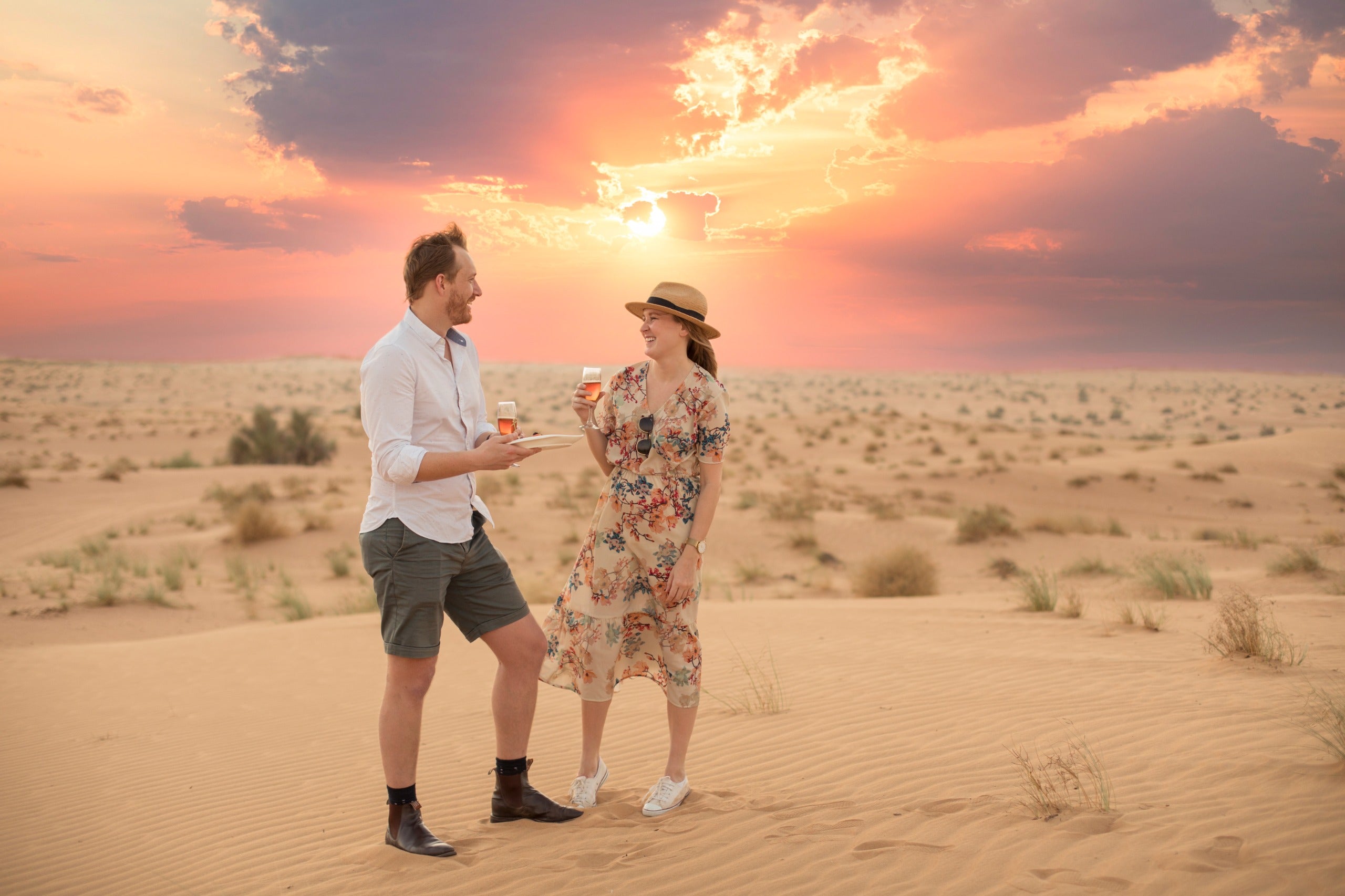 Man and woman standing in a desert landscape with a colorful sunset.